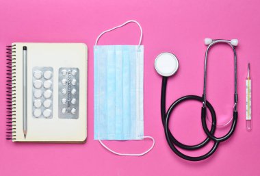 Tıbbi ekipman pembe bir arka plan üzerinde. Kabarcıklar hapları, Not defteri, stetoskop, termometre. Tıbbi kavramı, üstten görünüm, düz yatıyordu styl