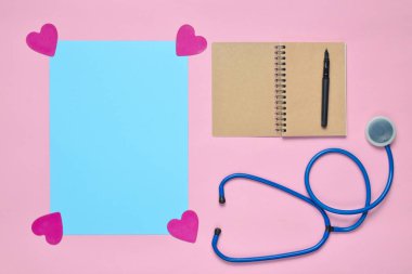Not defteri kalem, stetoskop, mavi kopya ile uzay pastel pembe bir arka plan üzerinde dekoratif yürekleri. Tıbbi kavramı. Üstten görünüm. Minimalis