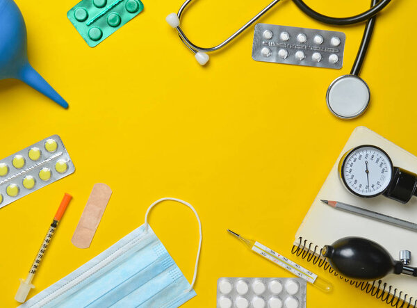 Medical equipment on a yellow background. Enema, blisters pills, notepad, stethoscope, syringe, thermometer, manometer. Medical concept, top view, flat lay style, copy space