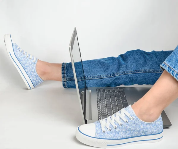 Vrouwelijke Benen Jeans Sneakers Een Laptop Een Witte Achtergrond Freelancer — Stockfoto