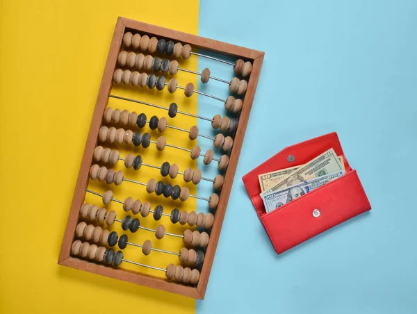 Retro wooden abacus, red leather purse with dollar bills on a colored paper background. top vie
