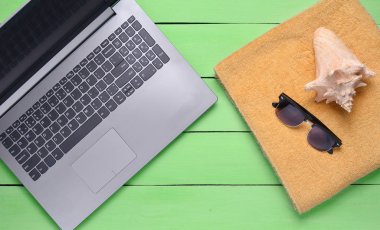 Online iş yerinde bir plaj tesisi. Dizüstü bilgisayar, havlu, güneş gözlüğü, kabuk, üstten görünüm, düz la