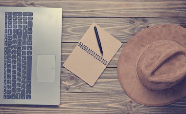 Dizüstü bilgisayar, keçe şapka, defter ve kalem ahşap bir masa üzerinde. Gazetecilik kavramı, üstten görünüm, düz la