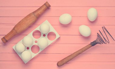 Pişirme işlemi. Çırpma teli pembe ahşap bir masa üzerinde plastik tepsi ile beyaz yumurta, oklava. Üstten görünüm