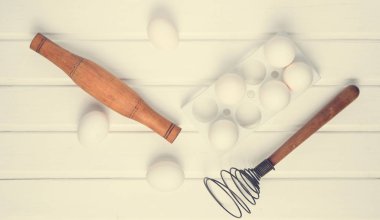 Pişirme işlemi. Beyaz ahşap bir masa üzerinde çırpma teli plastik tepsi ile beyaz yumurta, oklava. Üstten görünüm