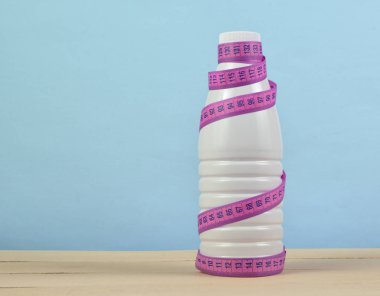 Bir cetvel üzerinde pembe bir arka plan, diyet, zayıflama concep yoğurt şişe sarılı