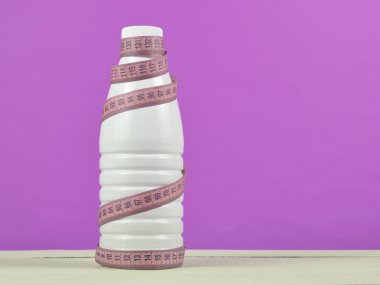 Bir cetvel üzerinde sarı arka plan, diyet, zayıflama concep yoğurt şişe sarılı