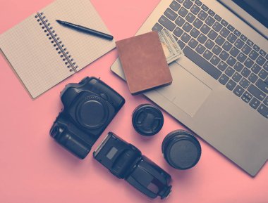 Ekipman fotoğrafçı, dizüstü bilgisayar, çanta ile dolar, defter pastel pembe bir arka plan üzerinde. Serbest kavramı, fotoğrafçının çalışmaları, nesneleri, üstten görünüm, düz la