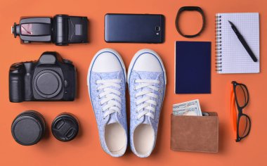 Becerikli ve aksesuarları düzen sarı bir arka plan üzerinde. Spor ayakkabı, fotoğrafik donanımlar, çanta ile dolar, akıllı saat, smartphone, defter, güneş gözlüğü. Seyahat, nesneleri, üst kavramı vie