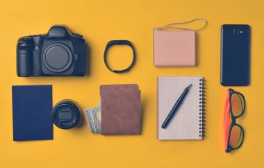 Becerikli ve aksesuarları düzen sarı bir arka plan üzerinde. Enerji banka, fotoğrafik donanımlar, çanta ile dolar, akıllı saat, smartphone, defter, güneş gözlüğü. Seyahat, nesneleri, üst kavramı vie