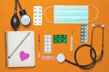 Sarı bir arka plan üzerinde tıbbi Kardiyoloji ekipmanları. Kabarcıklar hapları, defter, stetoskop, şırınga, termometre, manometre. Tıbbi kavramı, üstten görünüm, düz yatıyordu styl