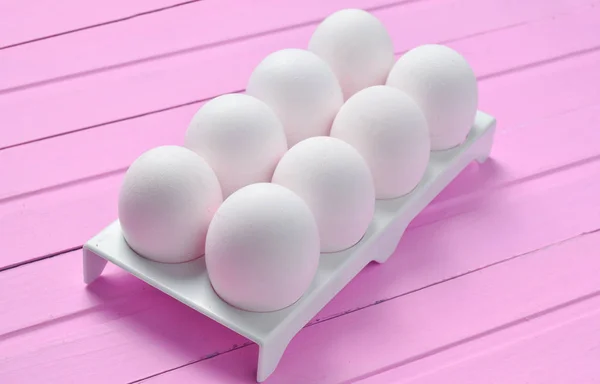 Plastic tray with white eggs on a pastel pink wooden table, minimalism tren