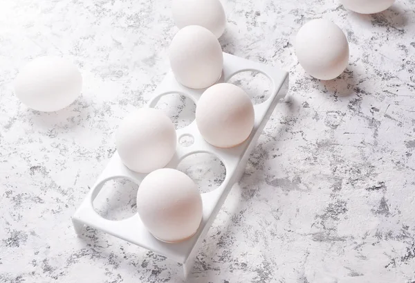 Plastic tray with white eggs on a white concrete backgroun