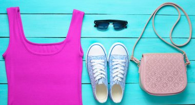 Kırmızı tişört, spor ayakkabı, deri çanta, mavi ahşap bir masa üzerinde güneş gözlüğü. Kadın giyim, Ayakkabı ve aksesuarları, üstten görünüm, la düz