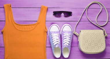 Kırmızı tişört, spor ayakkabı, deri çanta, mavi ahşap bir masa üzerinde güneş gözlüğü. Kadın giyim, Ayakkabı ve aksesuarları, üstten görünüm, la düz