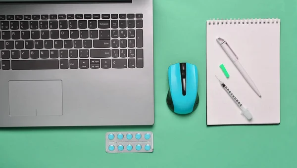 Workplace of a modern doctor. Laptop, wireless mouse, notebook, pills, syringe on a blue pastel background. Top view, minimalist tren