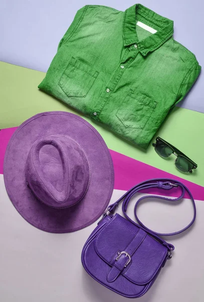 Women's fashion accessories and clothes. Denim shirt, felt hat, leather bag, sunglasses, layout on a colored background. Top view, flat la