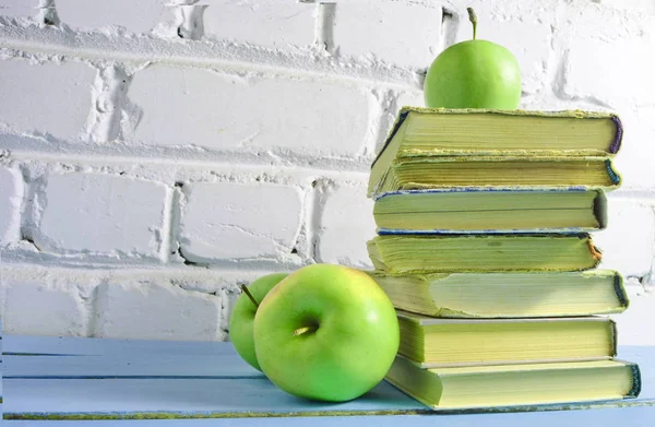Stack of old books, apple on a white brick wall background. School concept, education