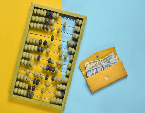 Retro wooden abacus, red leather purse with dollar bills on a colored paper background. top vie