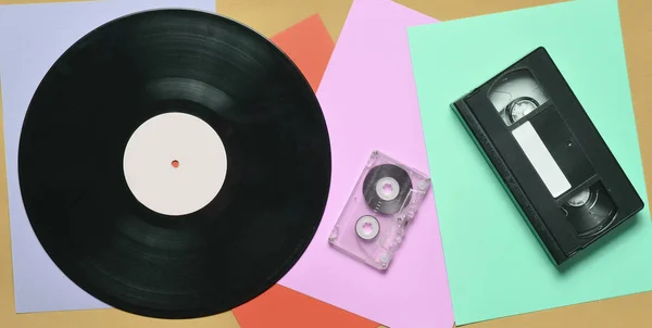 Vinyl record, audio cassette, video cassette on a multi-colored paper background. Retro style. top vie