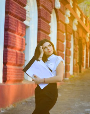 Beyaz bir bluz içinde çekici Bayan düşünceli kadar arıyor. Müdür antetli elinde tutuyor.