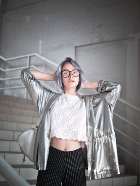  Uzay tarzı olağanüstü öğrenci kız külden mavi saçlı bir pelerin, gümüş rengi bir kumaş ve bir sırt çantası ile onun omuzlarında giyinmiş.