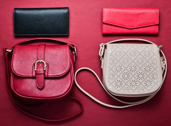 Fashionable lady accessories. Leather bags and stylish purses on a red background. Top view. Flat lay fashion.