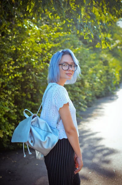 Cheerful blue-haired girl student with a briefcase of silver material one strolls through the park.