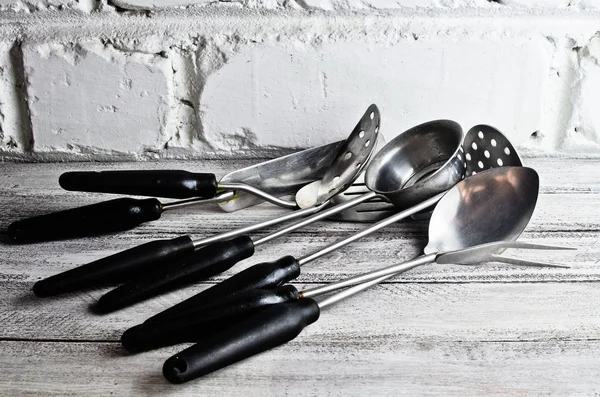 A set of kitchen tools for cooking against a white brick wall.