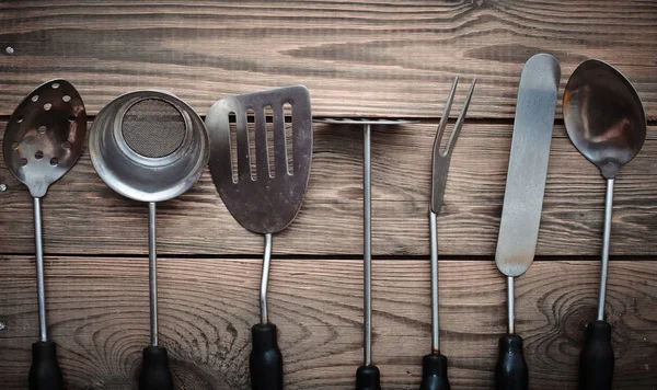 Set of kitchen tools for cooking from a sieve, fork, ladle, spoon, spatula for frying on a wooden table. Top view.
