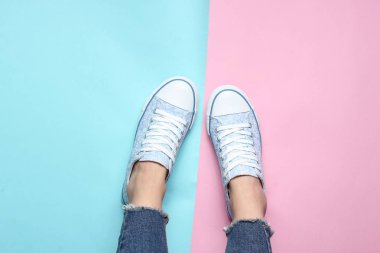 Kadın bacakları sıkı, yırtık kot pantolon, spor ayakkabı pembe mavi pastel arka plan üzerinde. Üstten Görünüm, minimalizm, kopya girintili