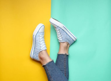 Kadın bacakları sıkı, yırtık kot pantolon, spor ayakkabı sarı mavi pastel arka plan üzerinde. Üstten Görünüm, minimalizm, kopya girintili