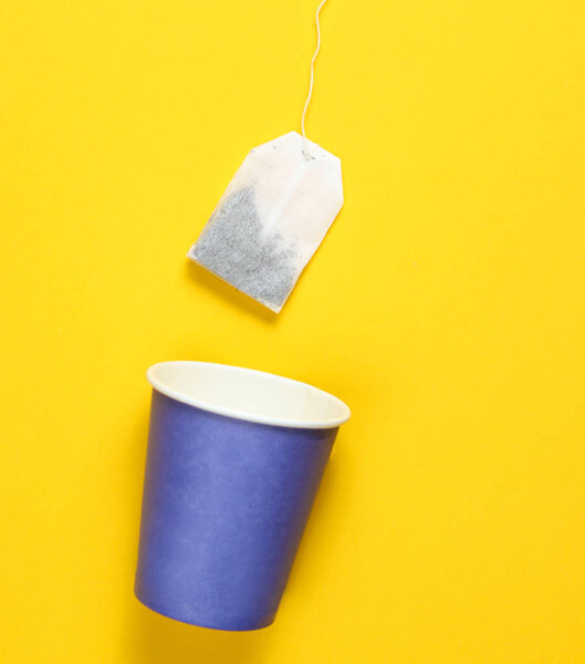 Empty disposable paper cup for tea, tea bag on a yellow background, top view, minimalis
