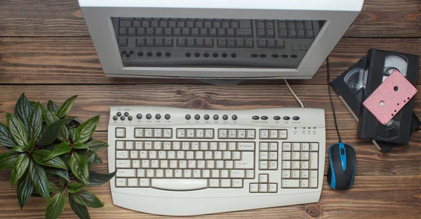 Retro computer on wooden table. Monitor, keyboard, pc mouse, pot with plant, video cassette, audio cassette, top vie