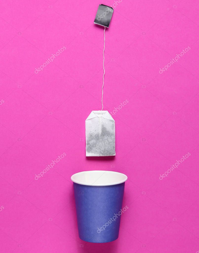 Empty disposable paper cup for tea, tea bag on pink background, top view, minimalis