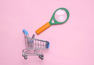 Magnifier, shopping trolley on pink patel background clipart