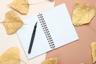 Not defteri ve kalem düştü yaprakları ile bej bir arka plan üzerinde. Ekim zaman, sonbahar ilham, gazetecilik, üst görünüm