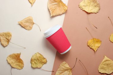 Kırmızı kağıt kahve bardağı ve bej kahverengi arka planda sarı yaprakları düştü. En iyi Vie