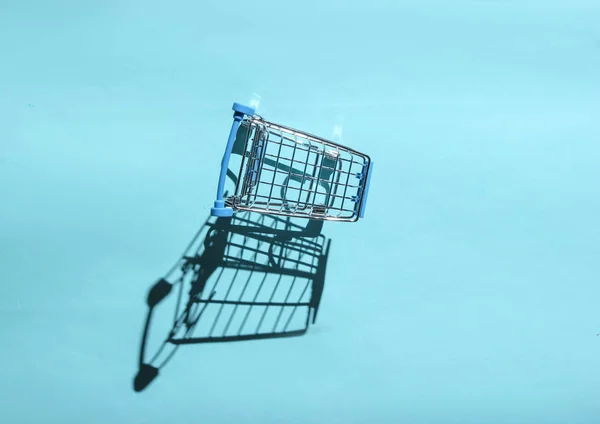 Mini shopping trolley for shopping on blue background, consumer concept, minimalism, top view, hard light, shado