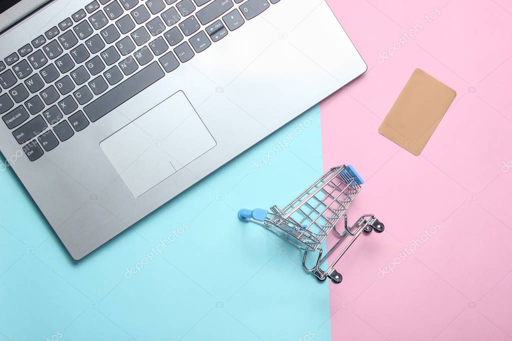 Mini shopping trolley, laptop, credit card on a colored pastel background. The concept of online shopping, top vie