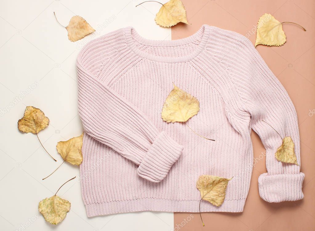 Fashionable sweater among the fallen yellowed leaves on creamy brown background. Autumn wardrobe. top view