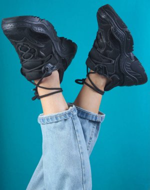 Mavi arka planda kot pantolon ve siyah spor ayakkabı bacaklar