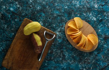 Soyulmuş çiğ patates, mavi beton arka plan üzerinde hazır kızarmış cips. Ev yapımı cips yapma süreci. Adım adım. Üstte görüntü.