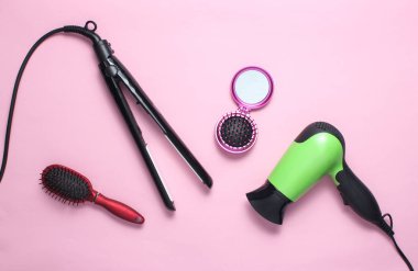 Saç kurutma makinesi, kıvırma demiri, saç fırçası, pembe pastel arka plan üzerinde ayna. Saç bakımı için güzellik ve moda nesneleri. Üstte görüntü