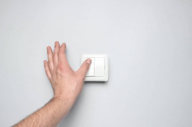 El, gri duvar arka planında bir ışık düğmesine basar