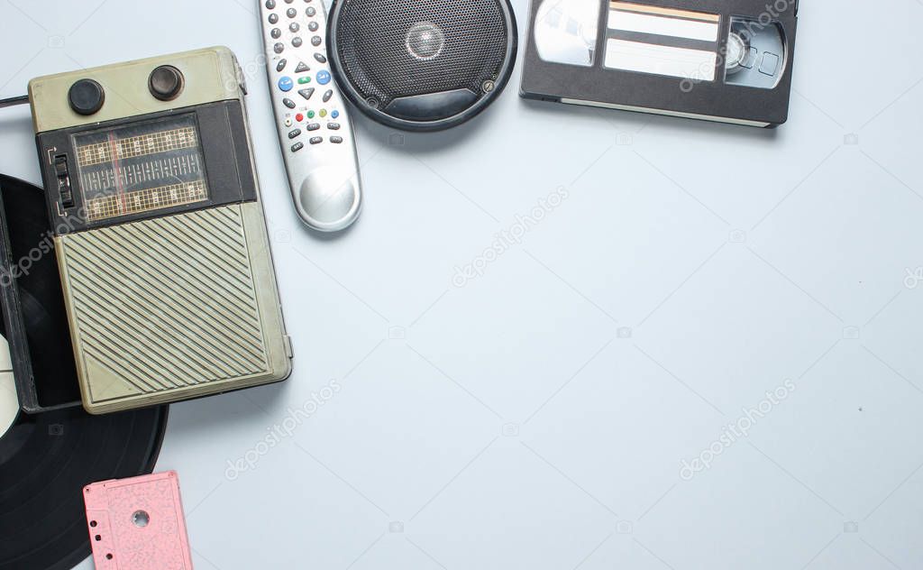 Radio receiver, vinyl record, audio cassette, video cassette, tv remote on a gray background. Top view, copy space