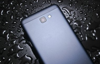 Su damlaları ile siyah bir arka plan üzerinde akıllı telefonun arka yüzü. Akıllı telefonunuzu wate'den koruyun