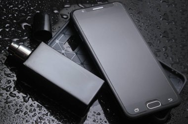 Koruyucu kılıflı akıllı telefon, su damlalı siyah arka plan üzerinde bir şişe erkek parfümü. İş ve moda concep