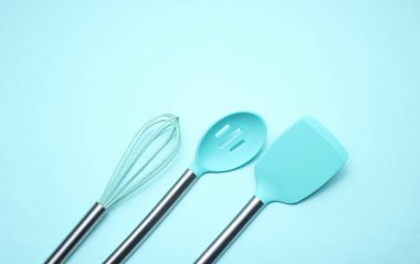 Mavi arka planda yemek pişirmek için araçlar kümesi. Metal saplı silikon kürekler, çırpma. Üst te. Kopyalama alanı