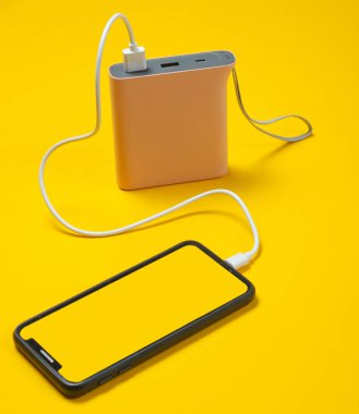 Modern akıllı telefon sarı arka plan üzerinde güç bankası ile şarj.
